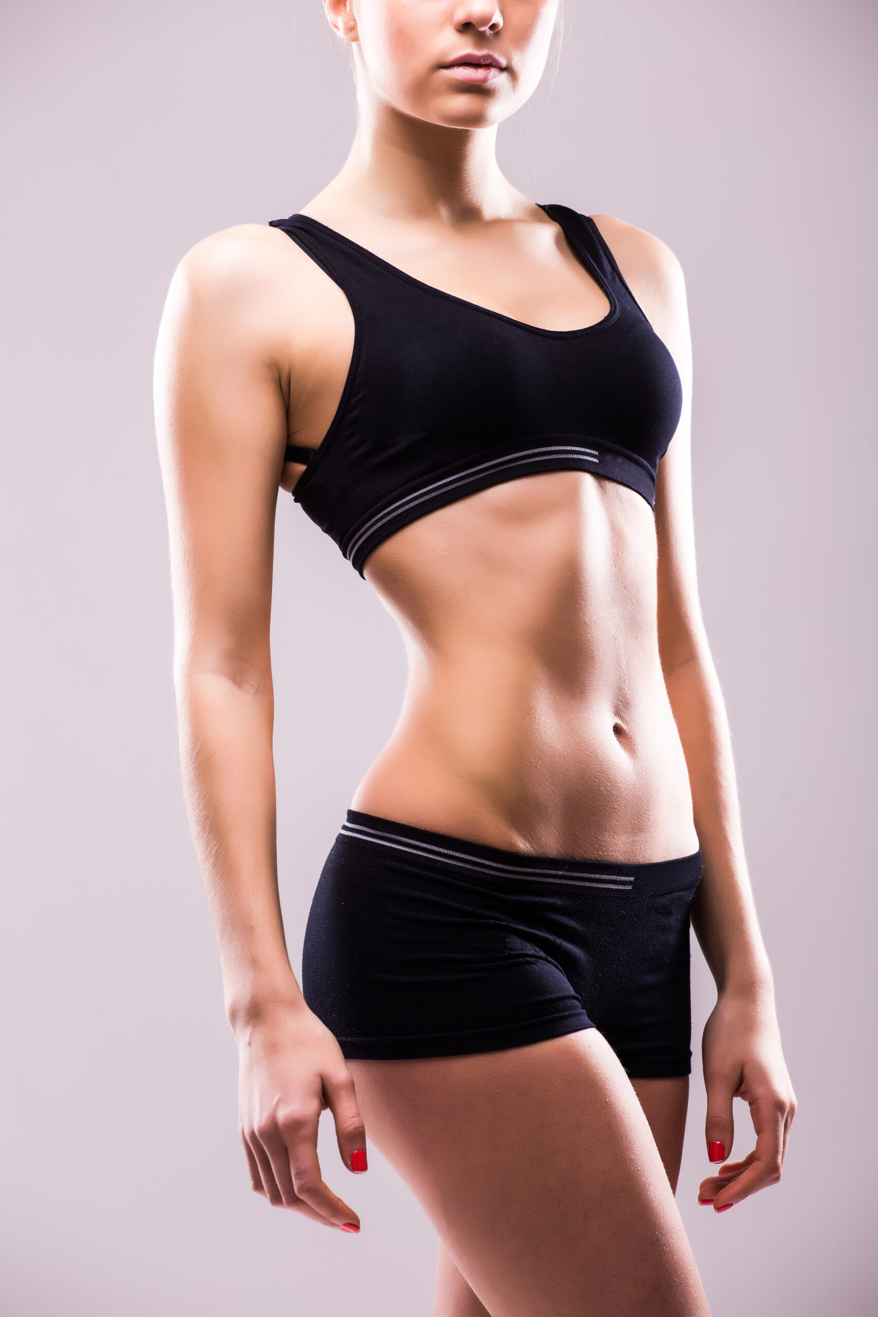 Muscular young woman athlete standing looking down with her hands on hips on grey background. Woman bodybuilder relaxing after exercise.